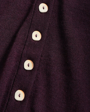 Close-up of a dark plum purple knit fabric with a vertical row of round off-white buttons.