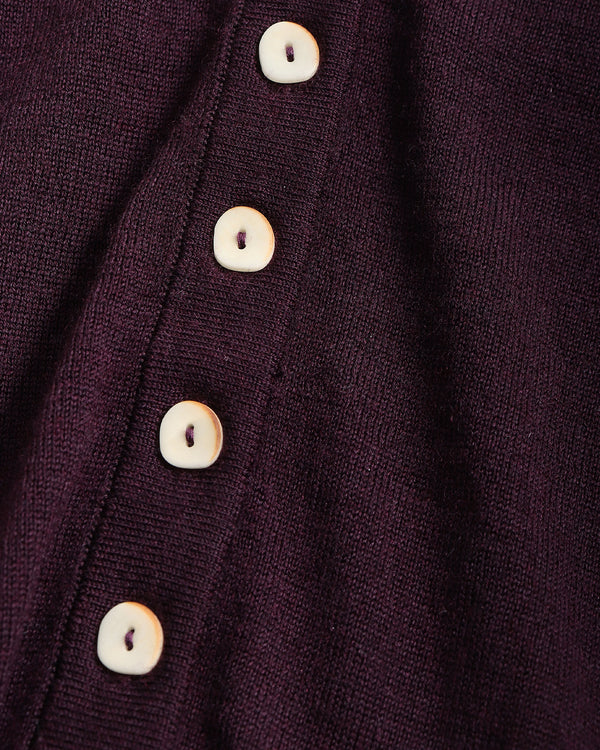Close-up of a dark plum purple knit fabric with a vertical row of round off-white buttons.