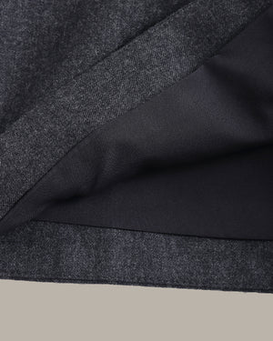 Close-up of a dark charcoal gray textured fabric with a smooth black lining, folded diagonally against a light beige background.