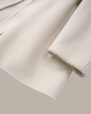 A close-up of a soft cream-colored fabric, likely wool or a wool blend, showing its brushed texture and a neat hemmed edge, set against a solid taupe background.