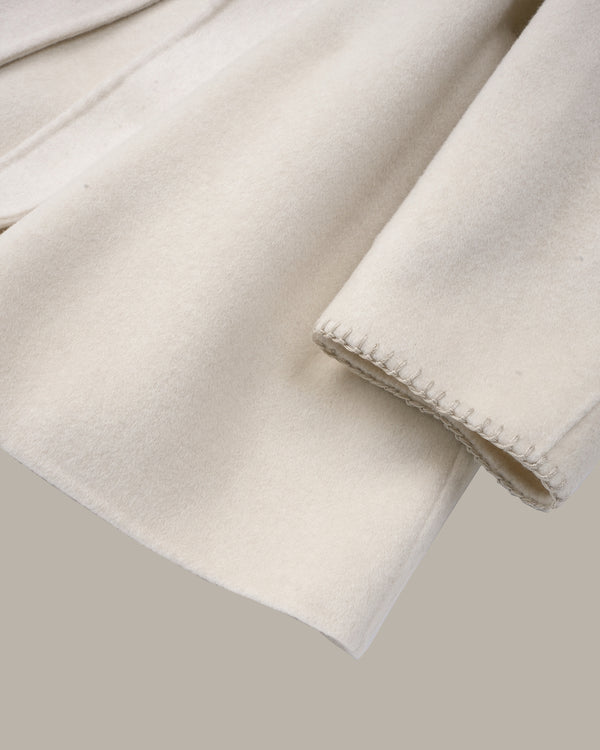 A close-up of a soft cream-colored fabric, likely wool or a wool blend, showing its brushed texture and a neat hemmed edge, set against a solid taupe background.