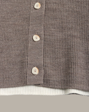 Close-up of a ribbed knit cardigan in taupe-brown with four light beige buttons and a white ribbed hem, shown against a neutral gray background.
