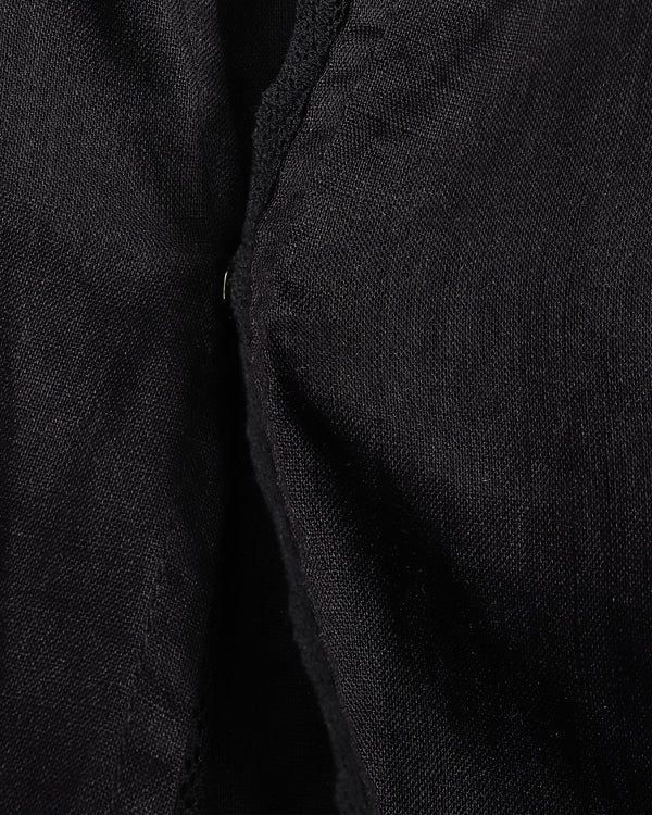 Close-up of a black textured fabric garment, showing a folded edge and fine woven material detail.
