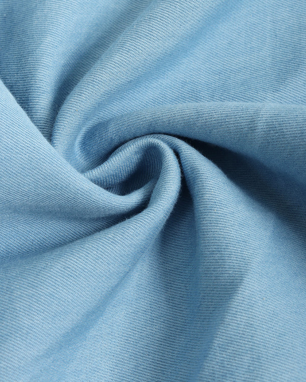 Close-up of a light blue sleeveless top or dress with a decorative white zigzag trim along the neckline, set against a solid taupe background.
