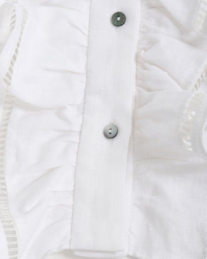 Close-up of a white ruffle top with buttons on a light gray background