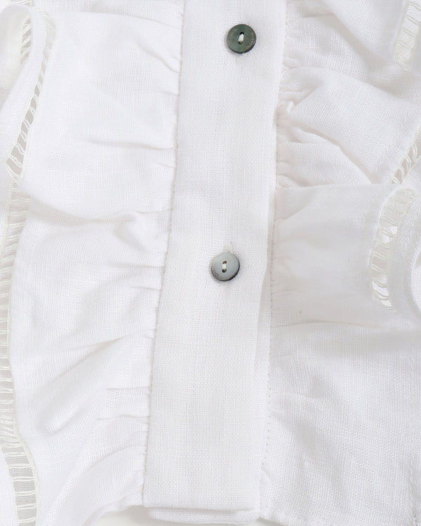 Close-up of a white ruffle top with buttons on a light gray background