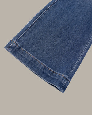 Close-up of a blue denim fabric cuff showing the hem and double-stitched edge against a solid beige background.