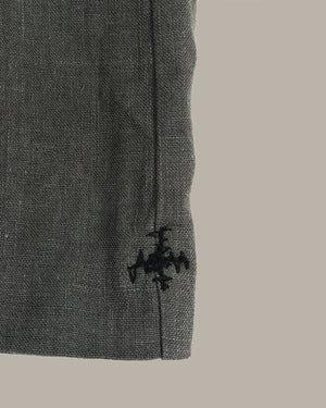 Close-up of a dark gray textured fabric sleeve or cuff with a black embroidered cross logo near the hem, set against a solid light gray background.