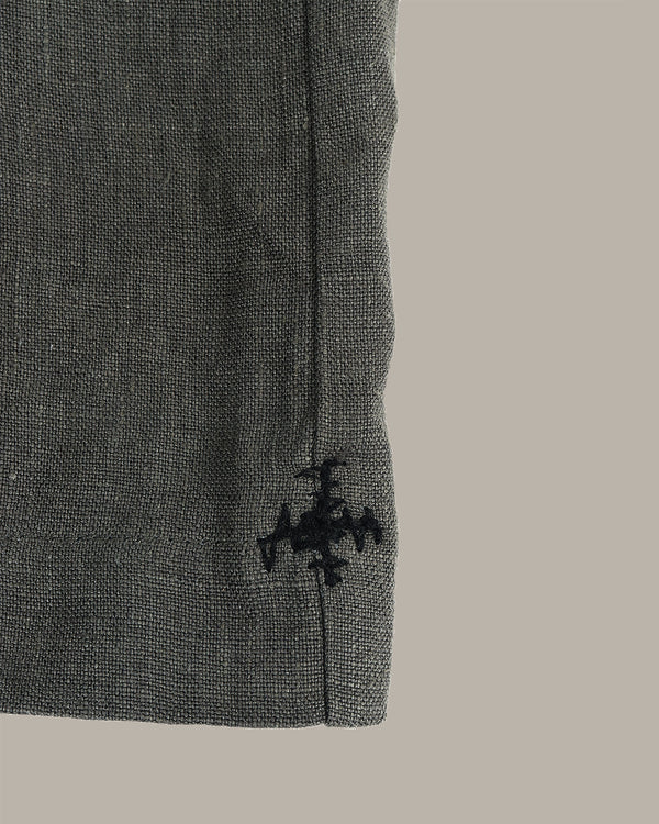 Close-up of a dark gray textured fabric sleeve or cuff with a black embroidered cross logo near the hem, set against a solid light gray background.