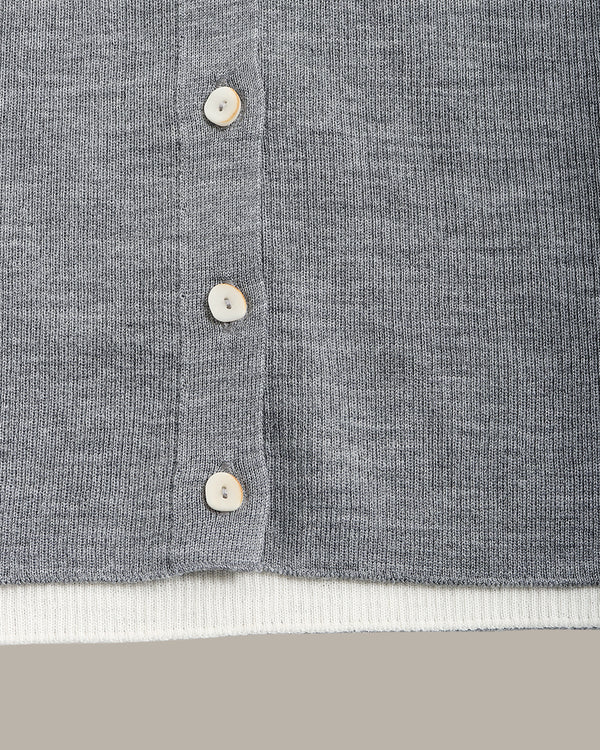 Close-up of a gray ribbed knit cardigan or sweater with a vertical button placket and white buttons, showing a white ribbed inner hem layer and a neutral beige background.
