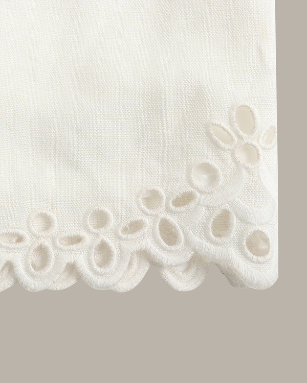 Close-up of a white fabric product corner with a scalloped eyelet embroidery border, shown against a light gray background.