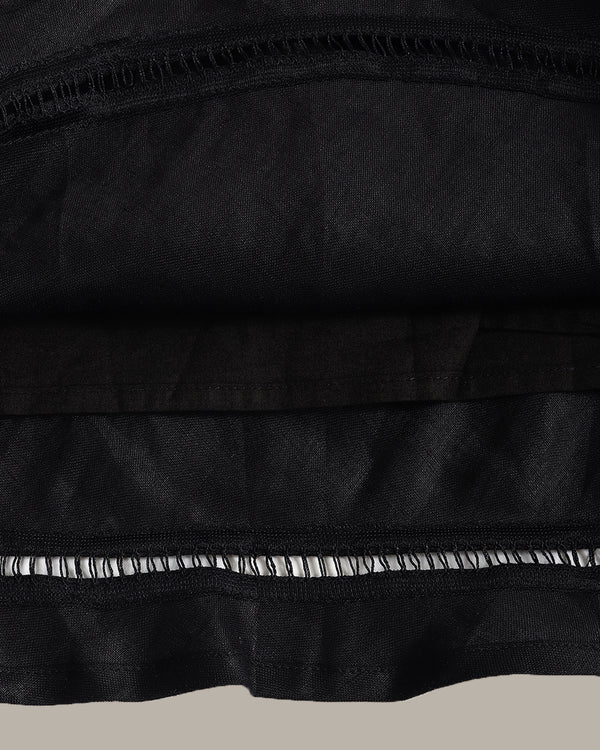 Close-up of a black fabric garment or textile with layered ruffles and a contrasting black-and-white striped ruffle trim, shown against a plain light gray background.