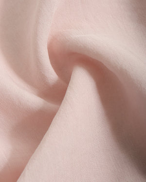 A close-up of soft blush pink fabric with gentle folds and a smooth texture.