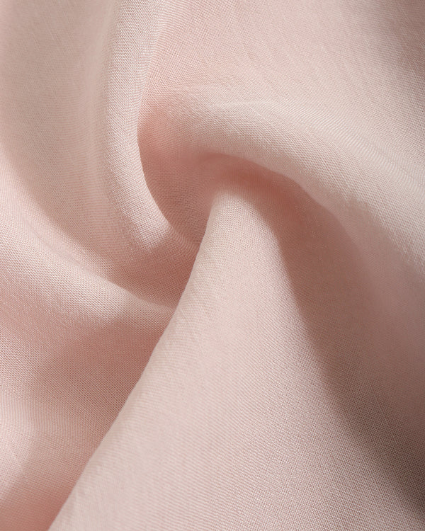 A close-up of soft blush pink fabric with gentle folds and a smooth texture.