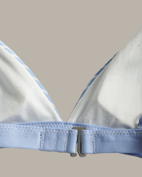 Close-up of a light blue and white bikini top showing the underband, adjustable strap, and metal clasp against a solid beige background.