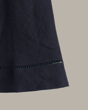 Close-up detail of a dark navy fabric garment or textile with a visible stitched hem, shown against a plain warm gray background.