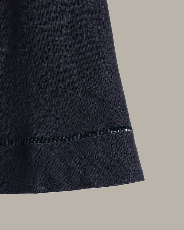 Close-up detail of a dark navy fabric garment or textile with a visible stitched hem, shown against a plain warm gray background.