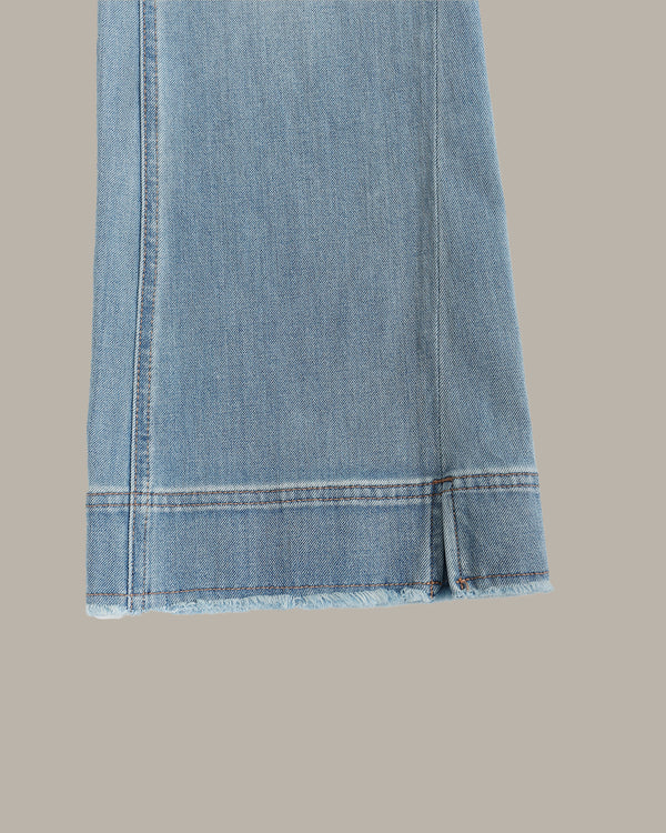 Close-up of a light blue denim garment, showing the hem with frayed edges and contrast stitching against a solid taupe background.
