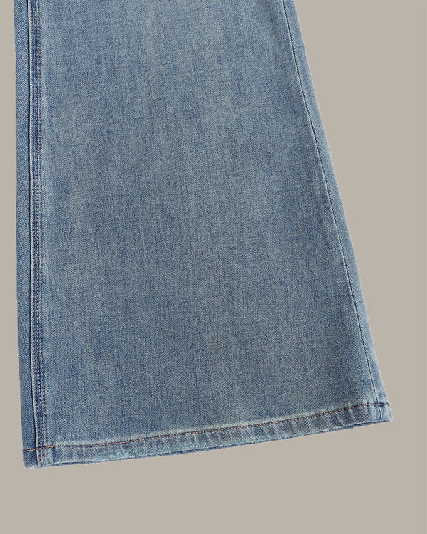 A close-up of a light blue denim fabric leg, showing the texture and hem stitching, set against a solid taupe background.