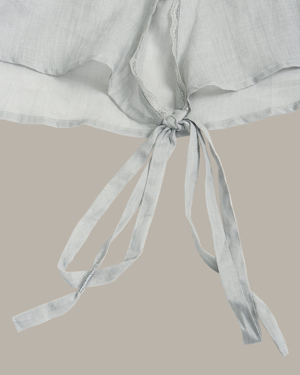 A close-up of a light gray or off-white textured fabric garment with a tie detail, shown against a solid warm beige background.