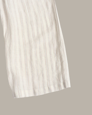 A close-up of a light cream or off-white striped fabric, likely a dress or long garment, shown against a solid taupe-gray background.