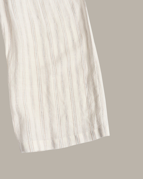 A close-up of a light cream or off-white striped fabric, likely a dress or long garment, shown against a solid taupe-gray background.